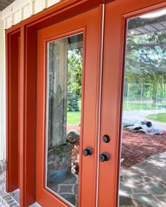 an orange front door with two glass panels on each side and a brick walkway in the background