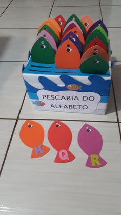 a box filled with different colored paper cutouts on top of a tiled floor next to a sign that says pescaria do alfabeto