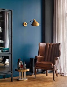 a living room with blue walls and leather chairs in front of a glass cabinet filled with liquor bottles