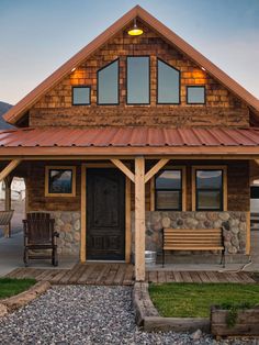 a wooden house with a metal roof and two benches in front of it on the grass