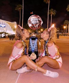 two women sitting on the ground kissing each other with a trophy in front of them