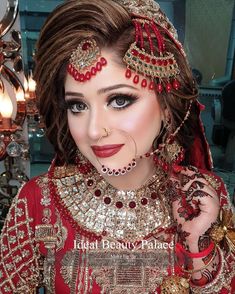 a woman in a red bridal outfit with jewelry on her head and hands near her face