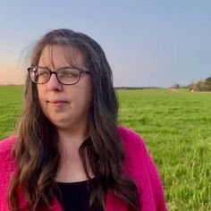 a woman wearing glasses standing in front of a field