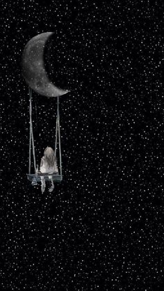 a person sitting on a swing in the dark with a half moon hanging from it's side