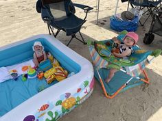 two babies are sitting in their baby bathers on the beach and one is playing with his toy