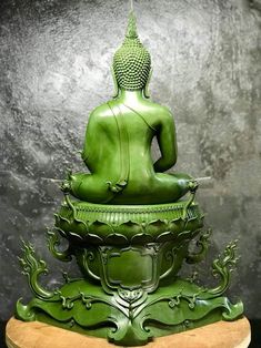 a green buddha statue sitting on top of a wooden stand