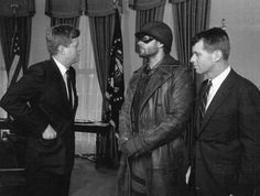 three men in suits and hats are talking to each other while standing in front of an american flag