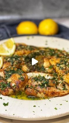 a white plate topped with chicken covered in pesto and lemons next to two lemon wedges