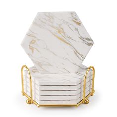 a stack of white marble coasters with gold metal handles on a white background in the shape of hexagon