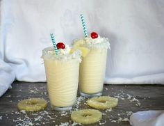 two glasses filled with milkshakes and topped with pineapples on a wooden table