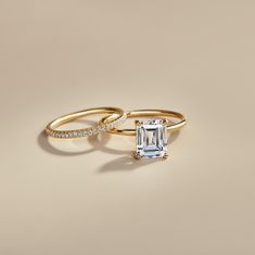 two gold rings with an emerald cut diamond on each one and a pave band around them