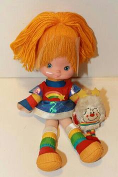 a doll with orange hair sitting next to a stuffed animal toy on a white surface