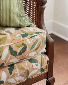 an upholstered chair with green and orange pillows on it's back, in front of a white wall