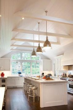 an open kitchen with white cabinets and wood flooring is pictured in this image, there are three pendant lights hanging from the ceiling