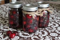 three jars filled with cherries sitting on top of a tablecloth covered table cloth