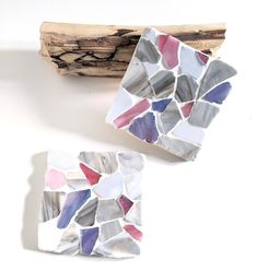 two pieces of mosaic tile sitting on top of a piece of driftwood next to each other