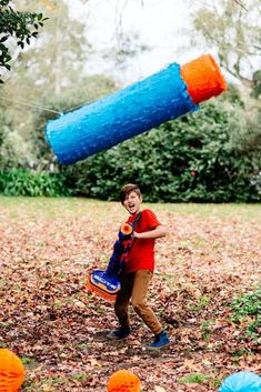 a young boy is playing in the leaves with an orange and blue object above him