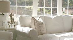 a living room with white couches and pillows in front of two large windows that look out onto the yard