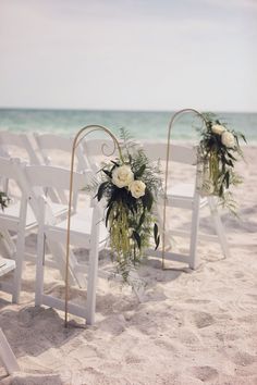 the chairs are set up on the beach for an outdoor ceremony with white flowers and greenery