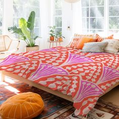 a bed with an orange and pink comforter on top of it next to a window