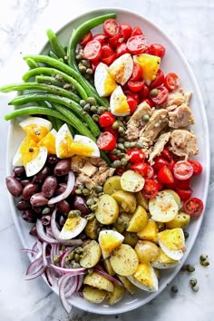 a white plate topped with meat, veggies and eggs next to green beans