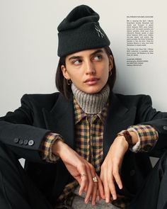 a woman sitting on the ground wearing a black hat and coat with her hands in her pockets