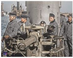 men in uniforms standing on a boat near the water and one man is operating a machine