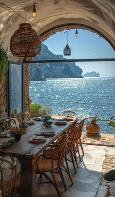 an outdoor dining area with table and chairs overlooking the ocean in front of large arched windows