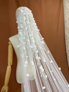 a white veil with flowers on it sitting next to a mannequin