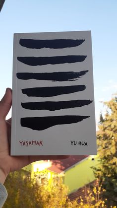 a person holding up a book with black ink on it in front of some trees