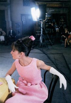 a woman sitting at a table in a pink dress with white gloves on her head