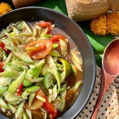 a bowl filled with lots of vegetables on top of a table next to spoons