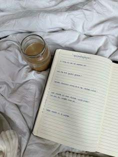 an open notebook sitting on top of a bed next to a cup of coffee