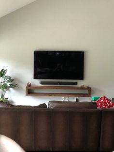 a large flat screen tv mounted on the wall above a brown couch in a living room