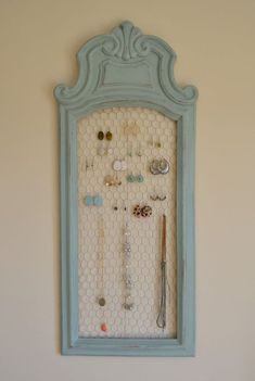 a blue frame with jewelry hanging from it's sides on the wall next to a white wall