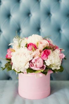 a pink hatbox with white and pink flowers in it sitting on a blue couch