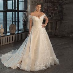 a woman in a wedding dress standing on a wooden floor next to a large window