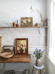 a room with a table, potted plants and pictures on the wall above it