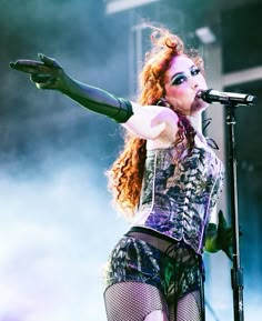 a woman with red hair and makeup on stage holding a microphone in her hand while wearing fishnet tights