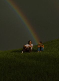 two people sitting in the grass with a rainbow in the background and one person holding a child