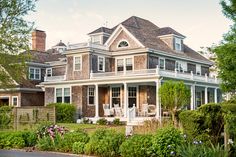 a large brown house with lots of windows and plants in the front yard, surrounded by greenery