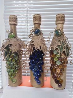 three wine bottles are decorated with glass beads and twine to look like grape vines