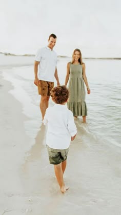 a man and woman are walking along the beach with their little boy in tow as they walk towards the water