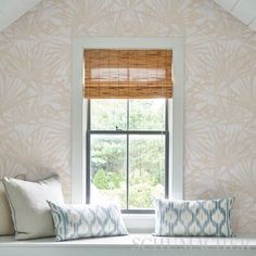 a window seat with two pillows on it in front of a wallpapered room