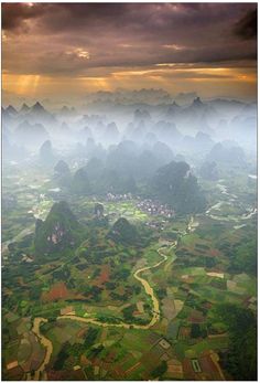 an aerial view of mountains and valleys in the distance, with clouds above them at sunset