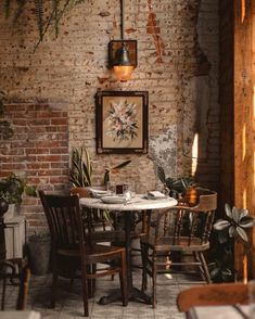 a table and chairs in a room with brick walls, potted plants and pictures on the wall