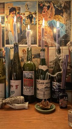 several bottles of wine on a table with candles in the middle and pictures behind them