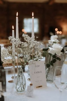 a table topped with lots of white flowers next to tall vases filled with candles