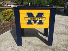 the michigan wolverines logo is painted on a wooden sign in front of a parking lot