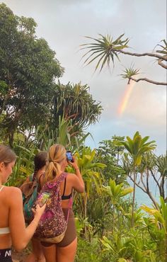 three women are standing in front of some trees and one is taking a photo with her cell phone